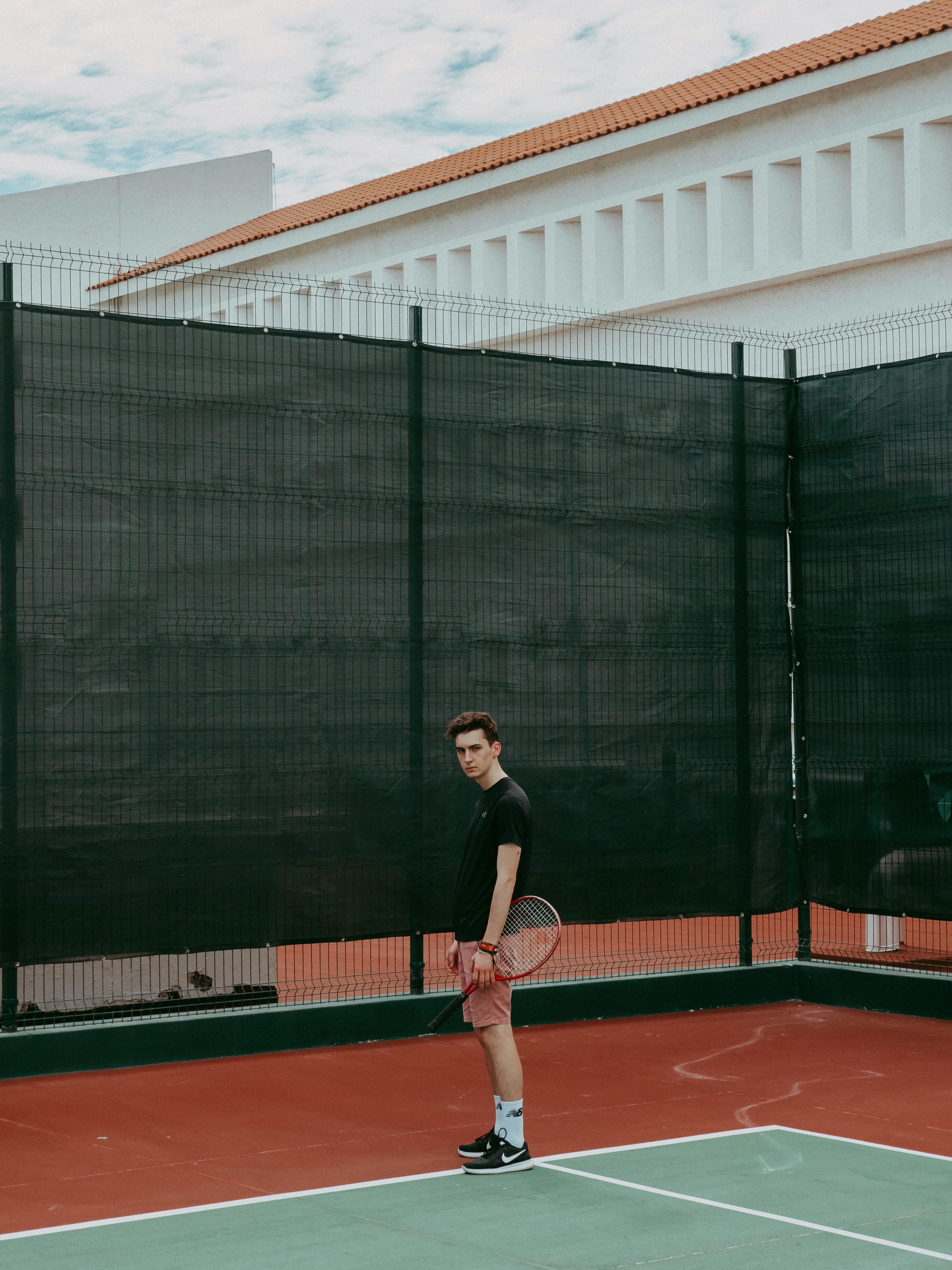 man in black shirt standing on red and white tennis court