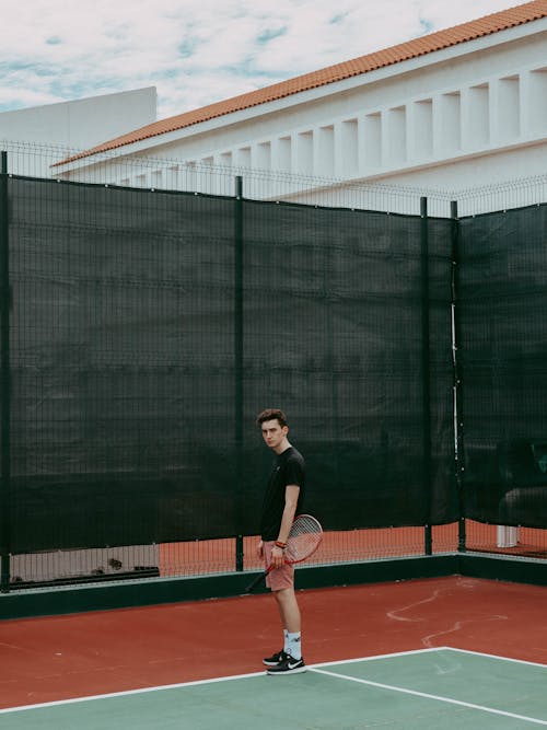 黑色襯衫站在紅色和白色的網球場上的男人