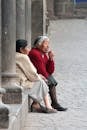 Woman in White Coat Sitting on Concrete Bench Beside Woman in Red Sweater