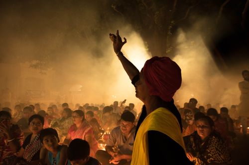 Free Side view of adult Indian female in traditional clothes and turban raising hand near crowd of people gathering at night during religious ceremony Stock Photo