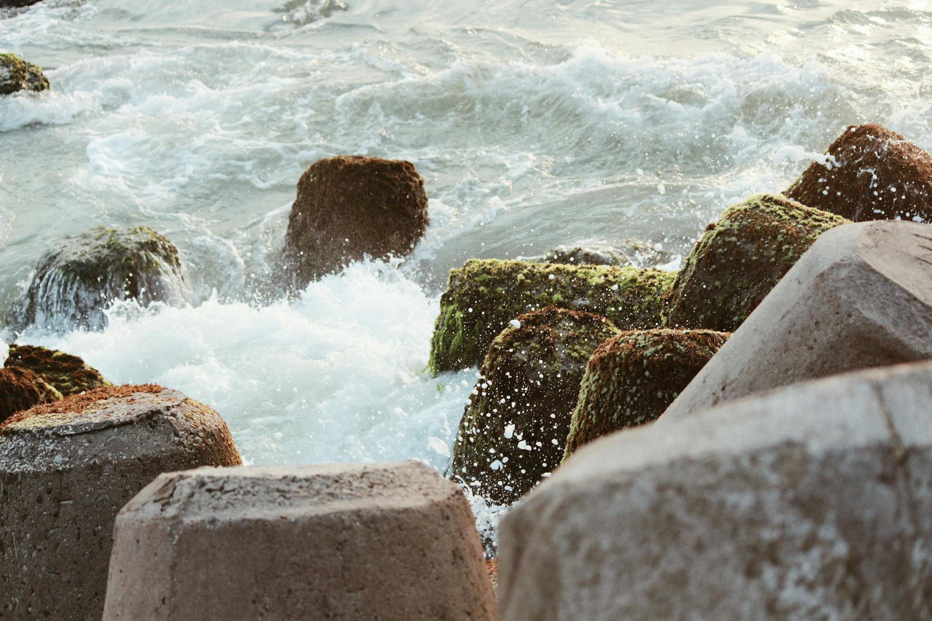 Dynamic ocean waves crash against moss-covered rocks, creating a scenic seascape.