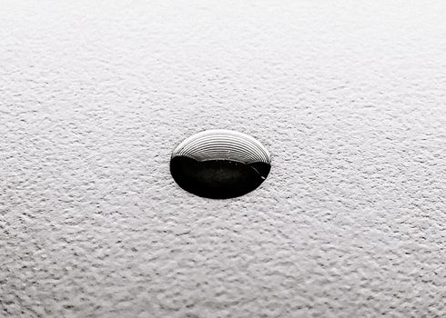From above of black and white rough surface with black liquid drop reflecting window with jalousie during daytime