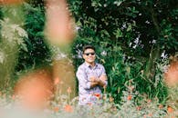 一位开朗的男子戴着太阳镜，在郁郁葱葱的绿叶和鲜艳的花朵间，享受着阳光明媚的一天