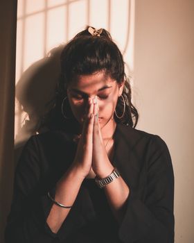 温暖的阳光下，一位年轻女子在室内闭目祈祷，姿态平静