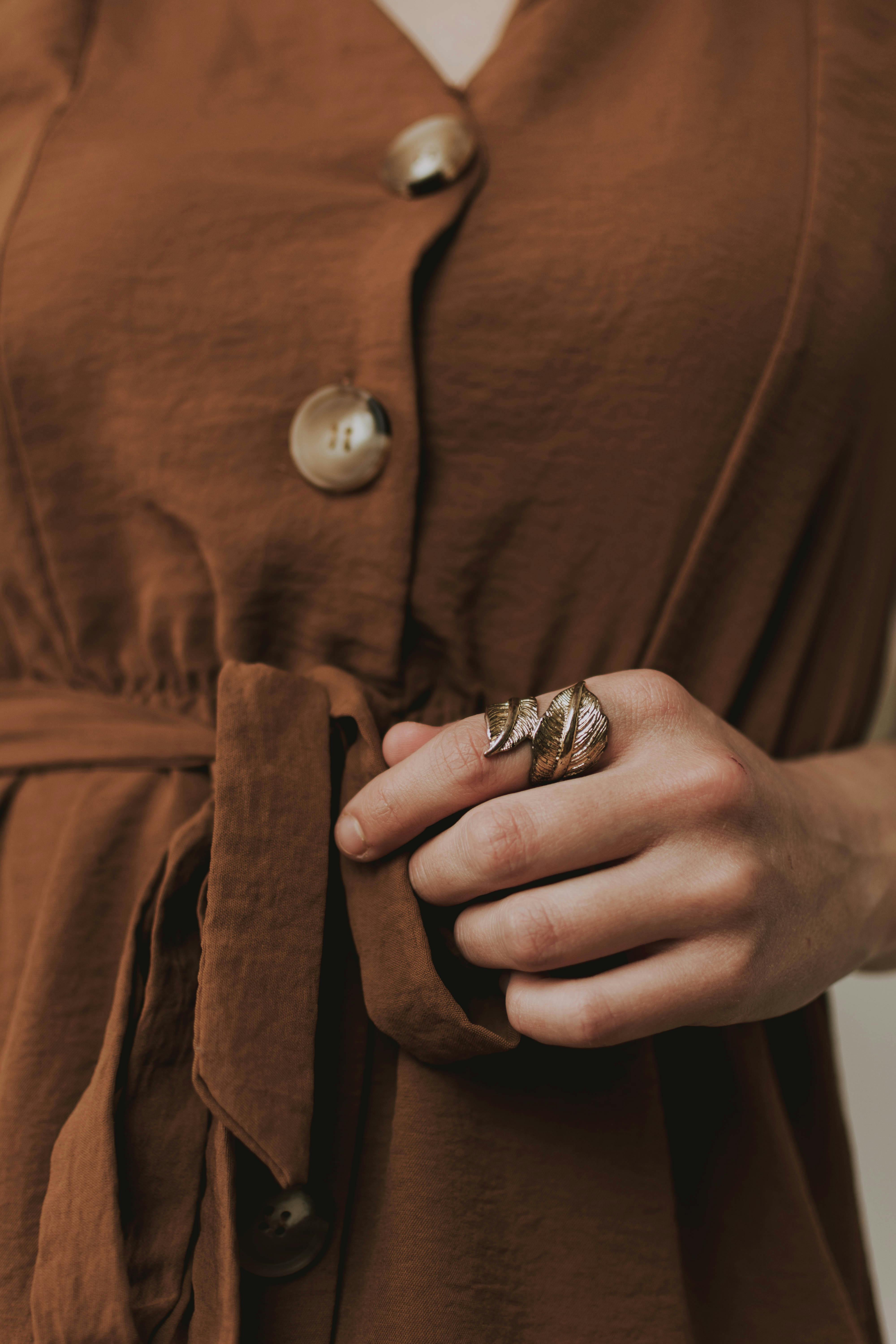 A close-up of a woman's hand with a stylish ring on a brown outfit, highlighting fashion and elegance.