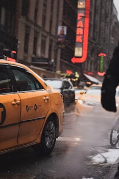 Yellow taxis navigate a rainy New York City street bustling with traffic.