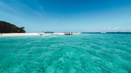 Free A serene tropical beach in Thailand with crystal-clear turquoise waters and boats under a blue sky. Stock Photo