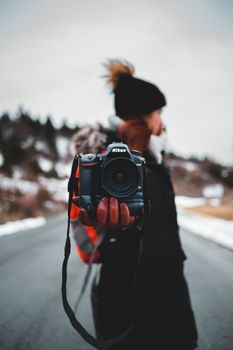 Blurred portrait of a female photographer holding a Nikon DSLR camera on a snowy road.