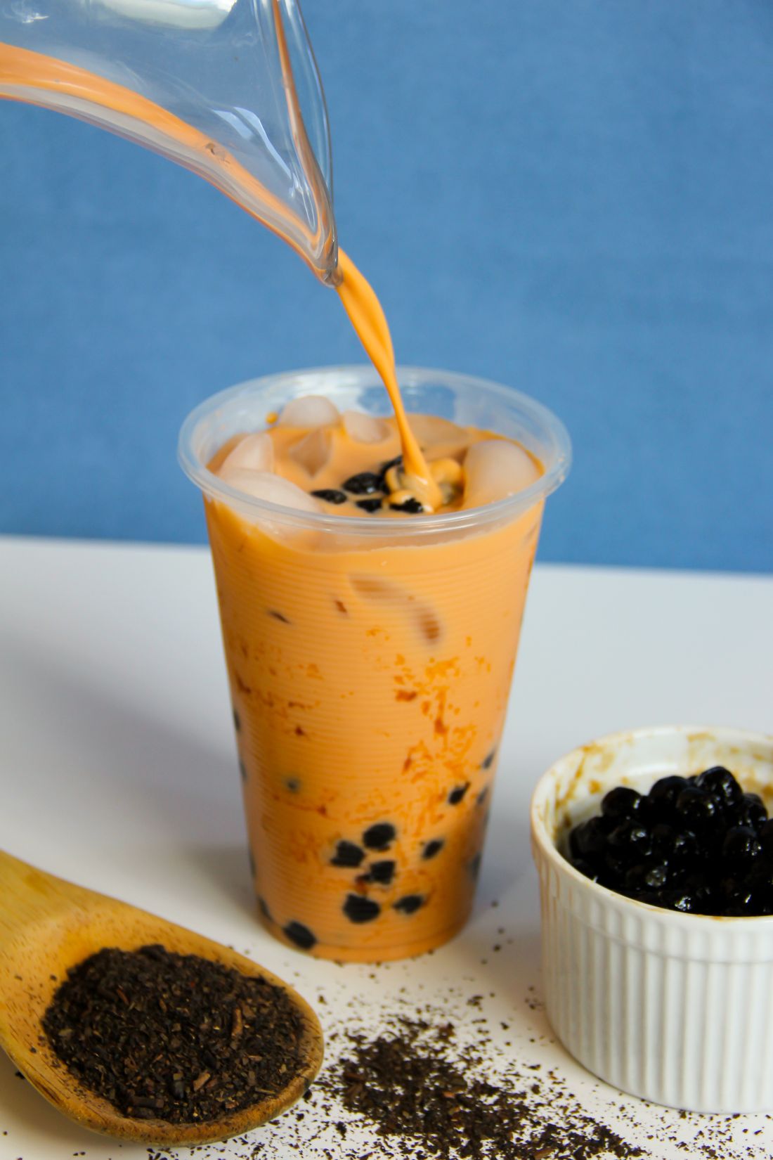 Thai milk tea being poured over ice and tapioca pearls in a logo-free cup