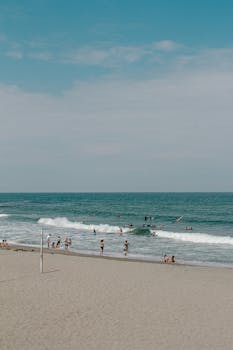 A lively beach scene with people surfing and swimming under the summer sun.