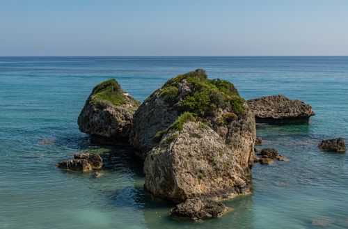 Free Scenic coastal rocks with green vegetation against the calm blue sea horizon. Stock Photo