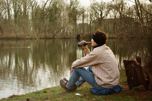 Free A person enjoying a peaceful moment by a lake, sipping a beverage with nature in the background. Stock Photo