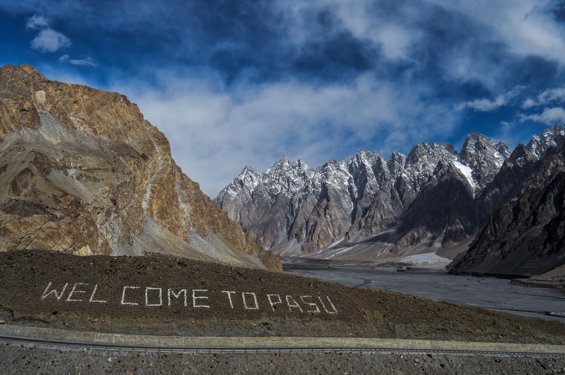 Snow-capped peaks and a scenic welcome sign in Pasu, Pakistan.