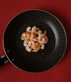 A top view of delicious prawns frying in a pan against a vibrant red background.