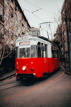 Retro red and white tram riding on narrow street amidst residential buildings and leafless trees in city