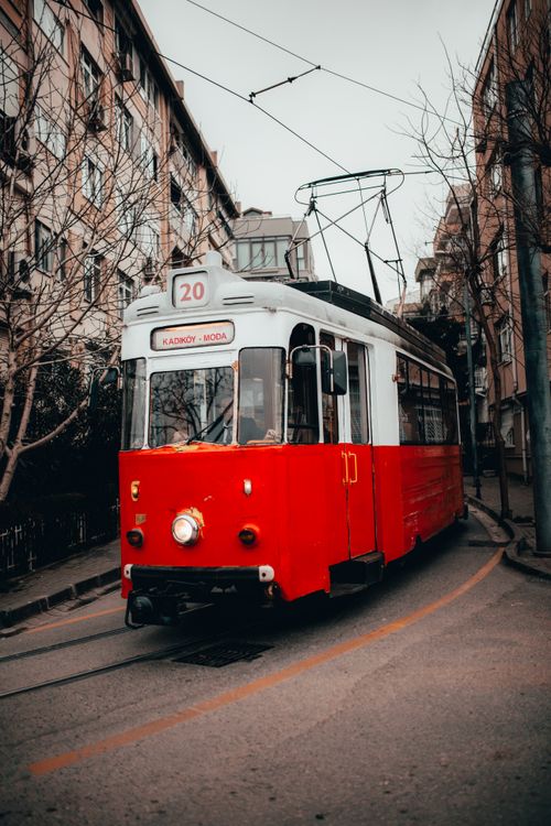 Free Retro red and white tram riding on narrow street amidst residential buildings and leafless trees in city Stock Photo