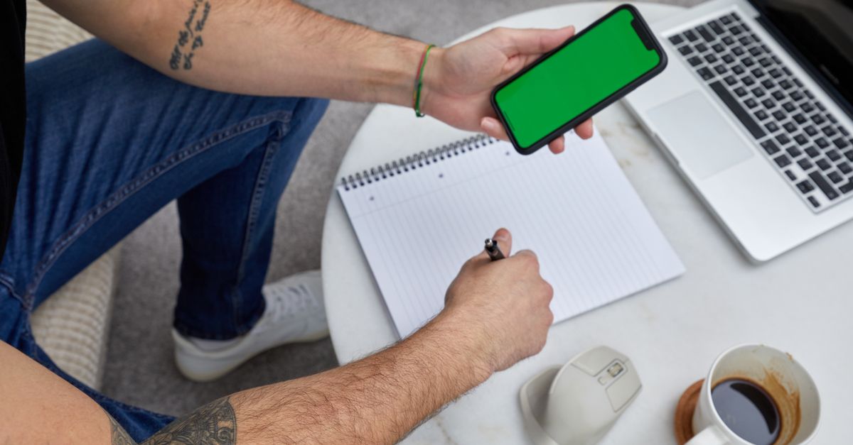 person writing in notebook with coffee and phone