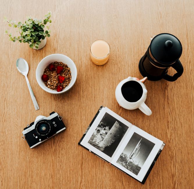 Overhead shot of a breakfast setup with coffee, granola, and a vintage camera on a wooden table.