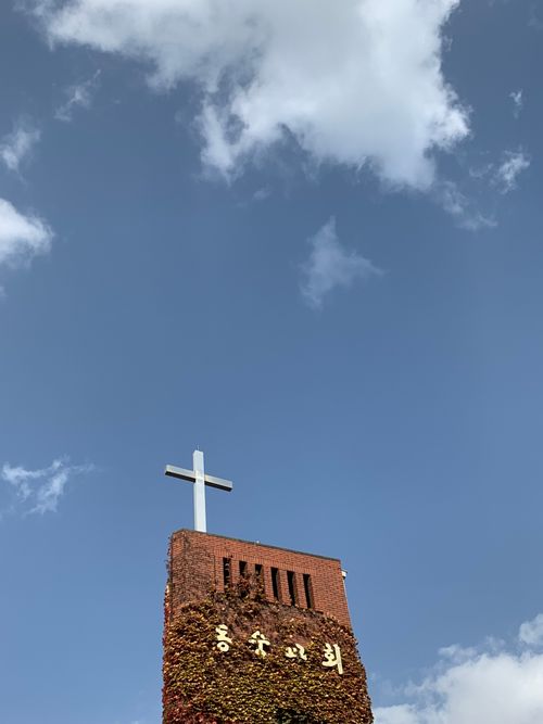 Free From below of ancient red brick tower with christian cross on top against blue cloudy sky Stock Photo