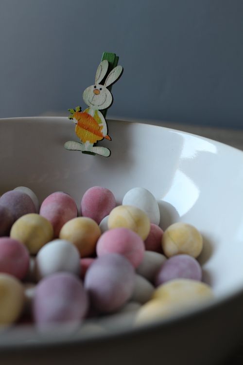 Free From above of white ceramic bowl with colorful candy eggs decorated with small wooden rabbit pin during Easter celebration Stock Photo