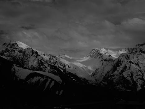 Stunning black and white photo of snow-capped mountains under dramatic clouds, perfect for nature lovers.