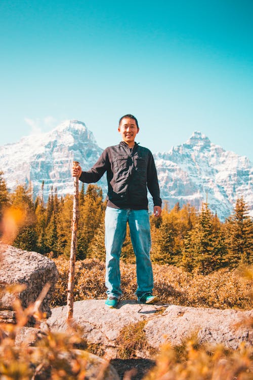 Man in Black Jacket Standing on Brown Rock Near Green Trees