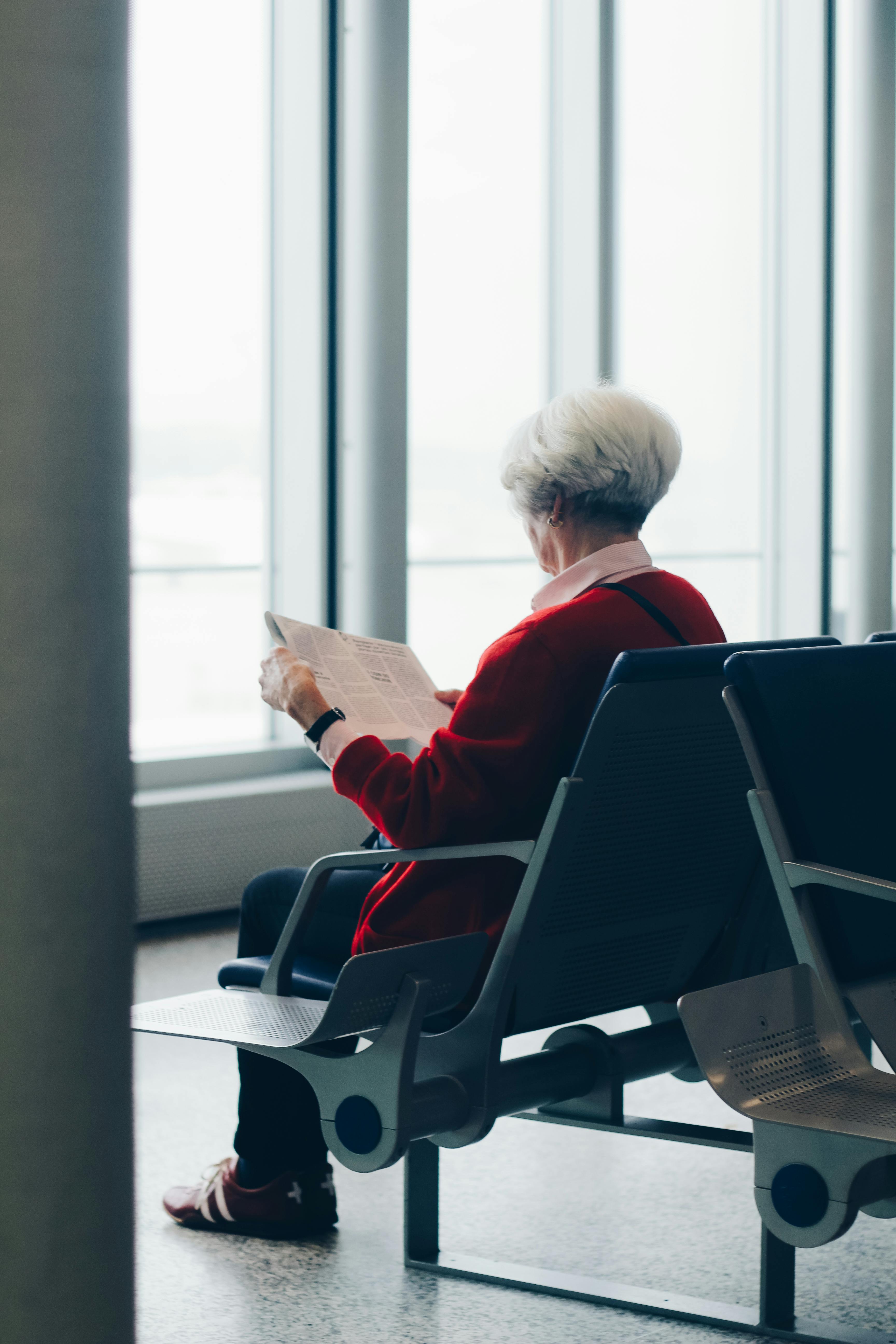 Old woman sitting on a chair while reading the newspaper. | Photo: Pexels