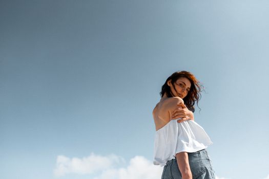 蓝天背景下，一位穿着白色衬衫和牛仔裤的女性低角度肖像