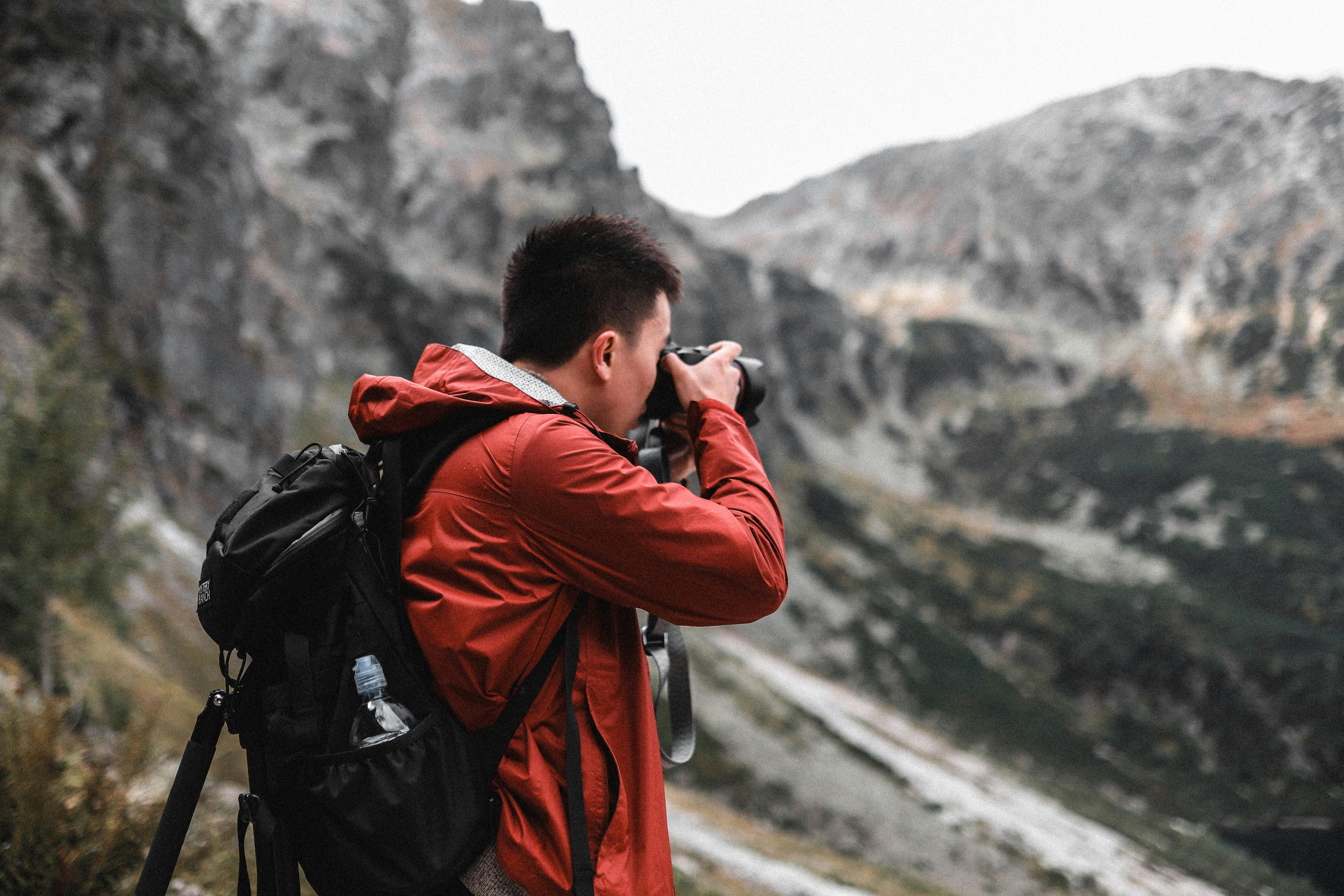 Photographer in a red jacket capturing mountain landscapes during a hiking adventure.