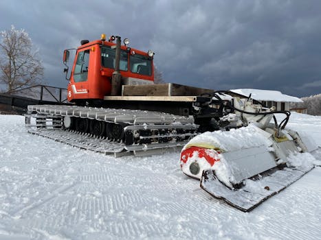 Red snow groomer machine preparing icy slopes for winter sports.