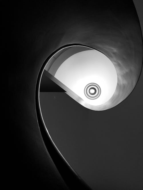 From below of black and white spiral geometric stairway inside modern minimal building