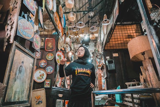 Low angle of young ethnic Muslim female customer in trendy outfit and traditional hijab choosing handmade goods in oriental souvenir shop