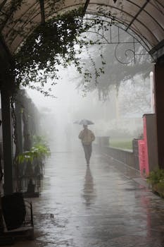 A person with an umbrella walks under an archway in foggy, rainy Gramado, Brazil.