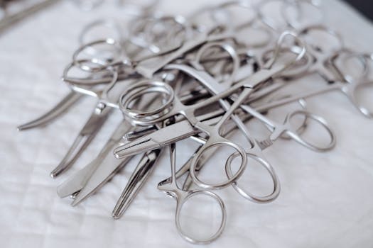 Close-up of a pile of stainless steel surgical tools, clean and sterile, on a white surface.