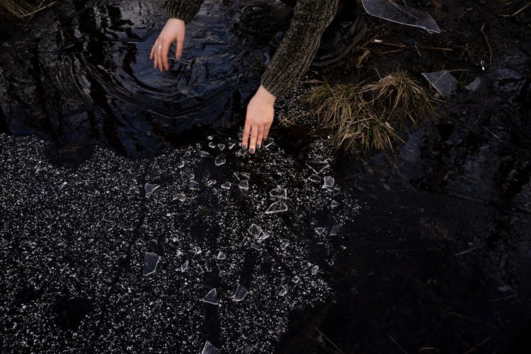 Crop Woman Picking Up Broken Glass Near Lake In Countryside