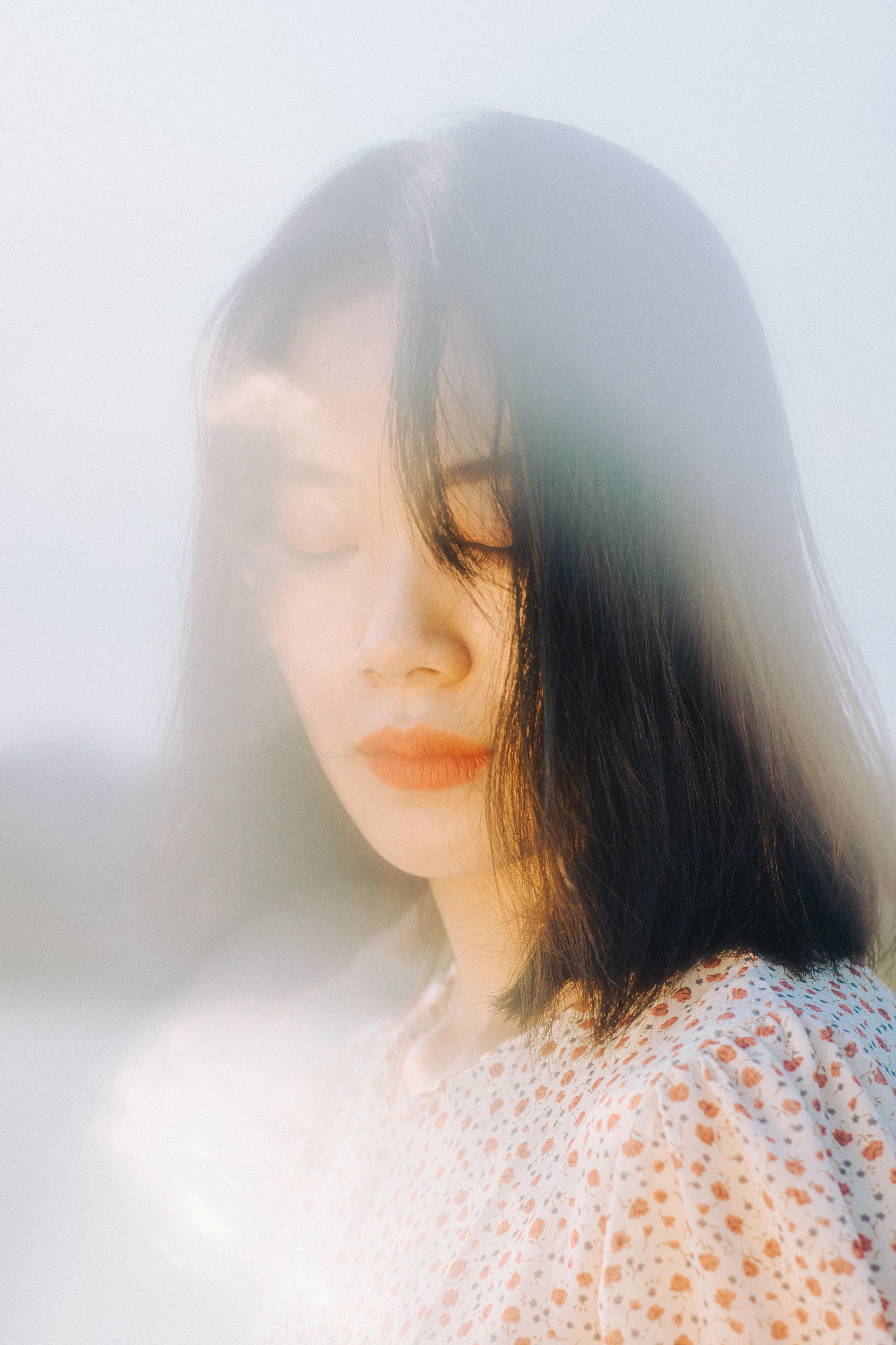 A serene portrait of an Asian woman with closed eyes, embracing a dreamy ambiance under natural light.