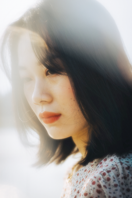 A dreamy portrait of an Asian woman in soft sunlight, evoking an ethereal and serene mood.