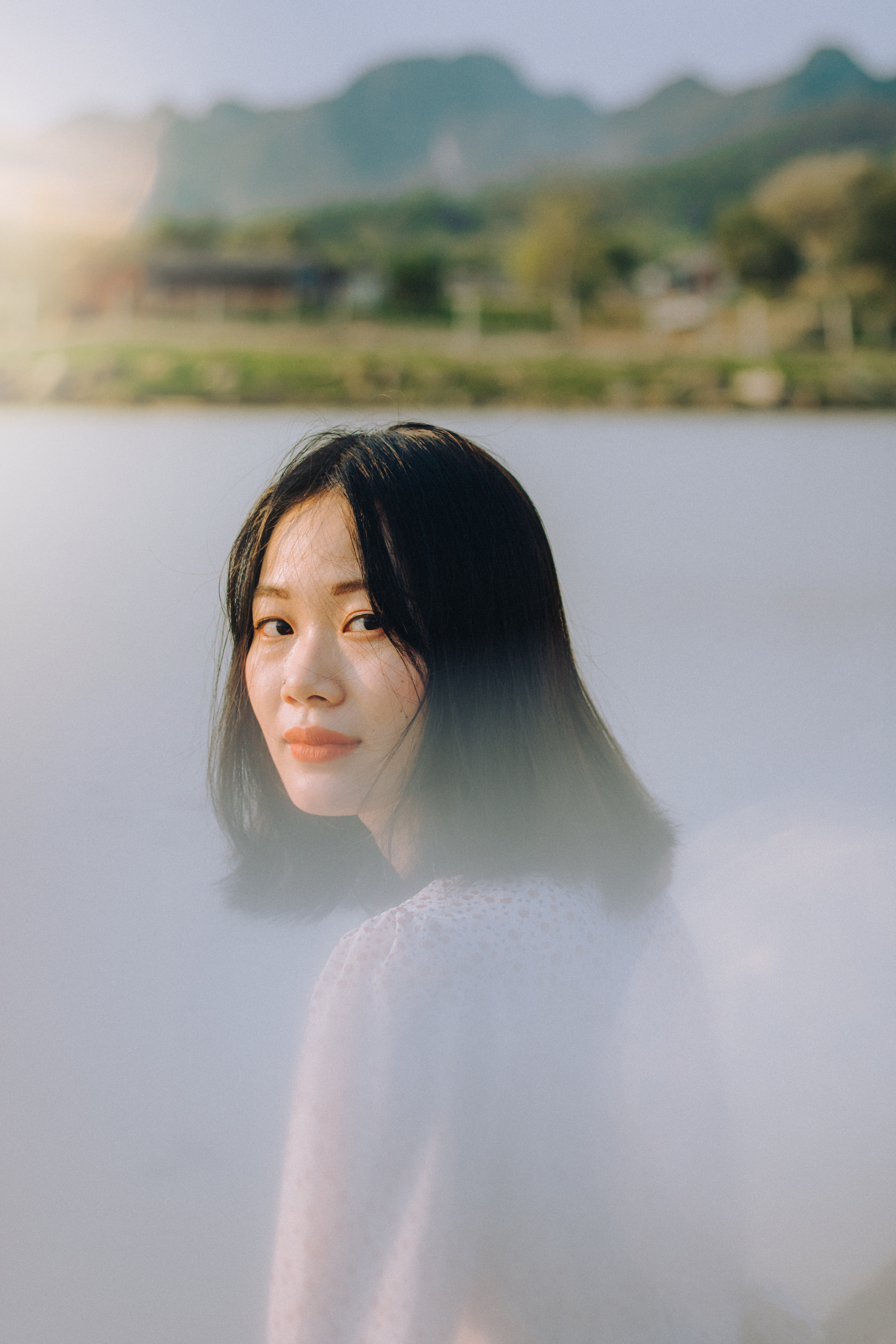 A serene portrait of an Asian woman near a lake in Vietnam, exuding dreamy and moody vibes.