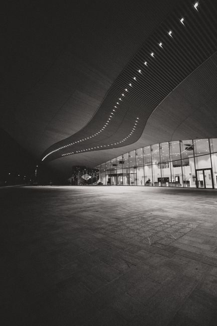 From below of black and white contemporary building with glass walls and illuminated overhang geometric roof at night