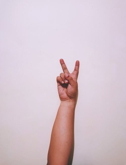 Free Crop anonymous person hand showing peace gesture against white background in light studio Stock Photo