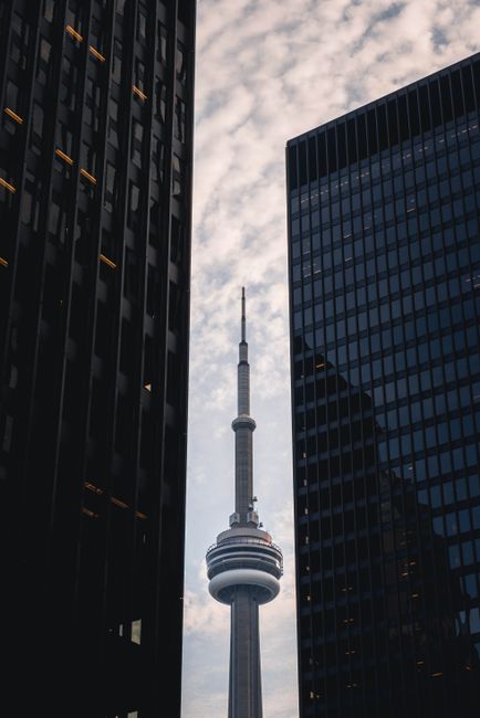From below of high famous CN Tower between modern skyscrapers with glass mirrored walls against cloudy sky in Toronto city