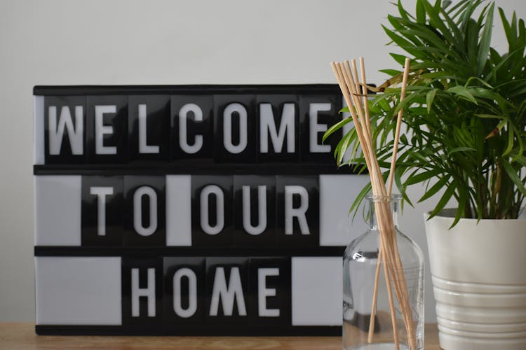 Potted Plant And Fragrance Sticks Placed On Table With Welcome To Our Home Sign