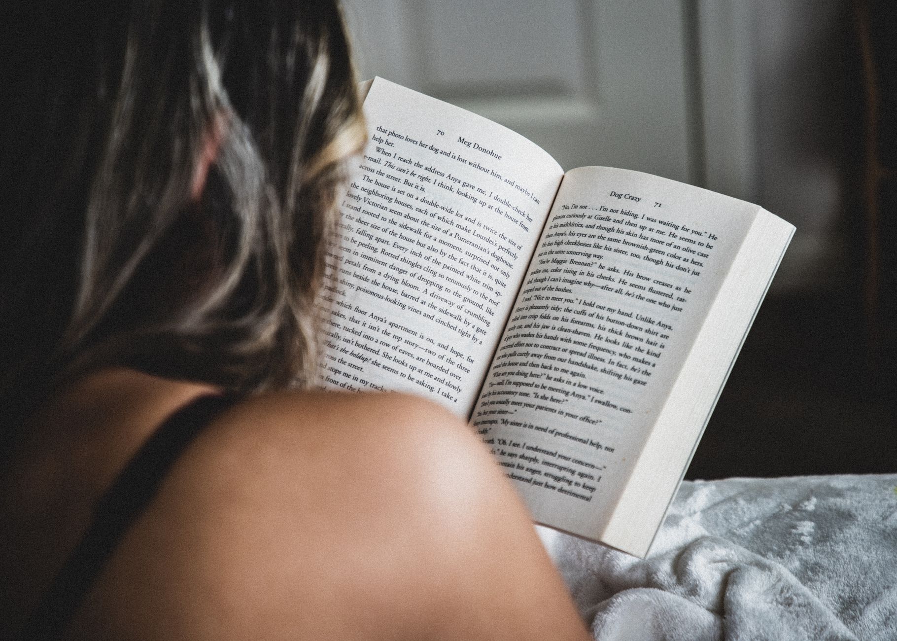 A woman reads a novel in bed, enjoying a quiet moment indoors, showcasing relaxation and literature.