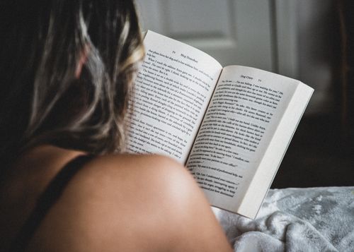 Free A woman reads a novel in bed, enjoying a quiet moment indoors, showcasing relaxation and literature. Stock Photo