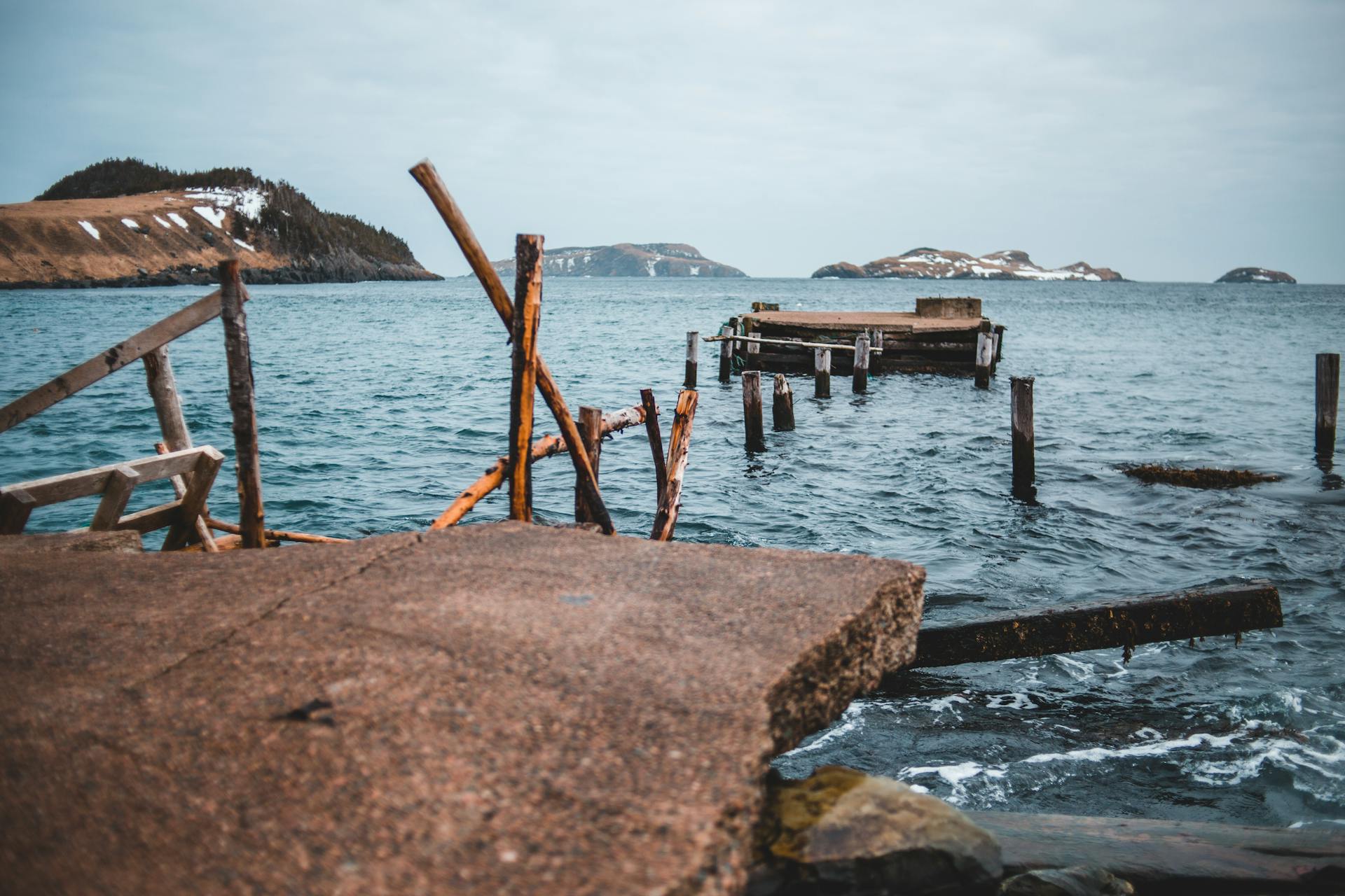Broken dock overlooking a serene ocean view with distant islands under a cloudy sky.