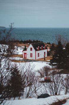 一座风景如画的白色小屋，点缀着红色，坐落在白雪皑皑的海岸线上