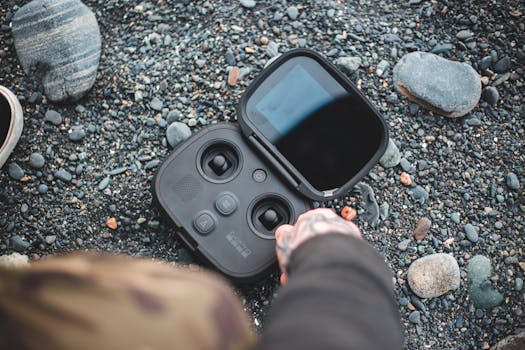 Close-up of a drone controller on a pebble beach, showcasing outdoor technology and leisure.