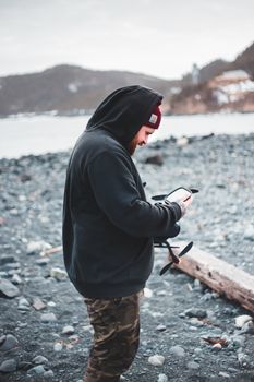 A man in a hoodie operates a drone on a rocky lakeside, showcasing outdoor adventure photography.