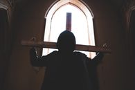 Silhouette of Man Holding a Cross Standing Near Window