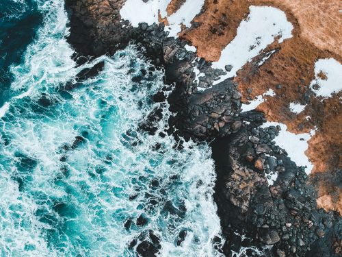 Free Stunning aerial shot of Tors Cove, NL with waves crashing against a snowy shoreline. Stock Photo